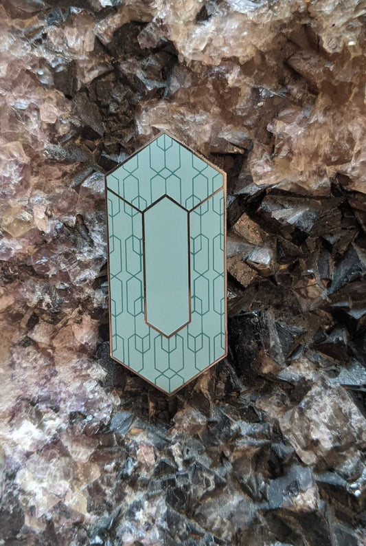 A light blue enamel pin with an elongated diamond shape, with a decorative pattern